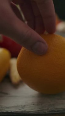 Masadaki çeşitli sebze ve meyvelerin arasında isimsiz biri tarafından olgunlaşmış portakala yakınlaşıp uzaklaşan kamera. Dikey çekim.