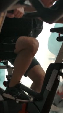 Beyaz erkek ve bayan sporcular spor salonunda arka arkaya egzersiz bisikletleri üzerinde bacak kaslarını çalıştırıyorlar. Gençliği koruma arzusu. Bacaktan yüzlere dikey tava. Dikey çekim.