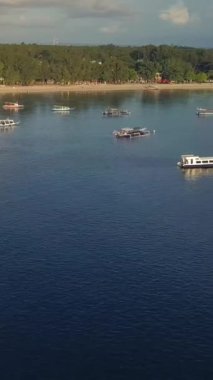 Tropik ada havası. Lombok, gili. Güneşli bir günde, okyanustaki tropikal adanın kıyısındaki su üzerindeki teknelerin güzel manzarası. Paralel kayan dikey çekim.
