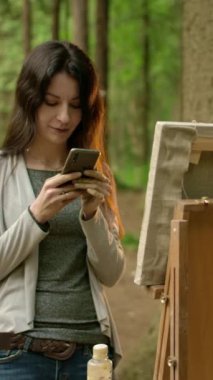Genç esmer kadın akıllı telefonuyla mesaj atıyor. Parktaki kız ressamın orta manzarası. Dikey çekim.