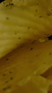 Karanlık odada kameranın önünde dönen tırtıklı desenli yakın plan patates cipsi. Dikey çekim.