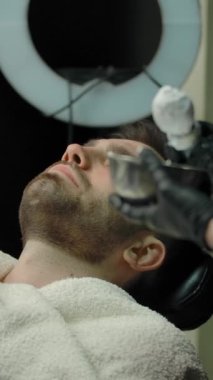 Kadın kuaför müşterinin sakalına tıraş köpüğü sürüyor. Modern moda bir berber dükkanında müşteriyi jiletle tıraş olmaya hazırlamak. Dikey çekim.