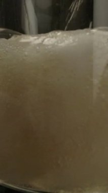 Karanlık odada yavaş çekimde cam bardağa dökülen köpüklü taze bira. Dikey çekim.