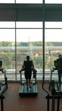 Spor salonunda koşu bandında koşan üç sporcu, iki erkek ve kadın. Yüksek bir yerden ateş etmek, uçmak. Boş spor salonu. Dikey çekim.