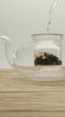 Çaydanlıktan kaynamış suyu, ahşap bir masada, kuru beyaz bir çaydanlığa döküyorum. Makro dolly yavaş çekim dikey çekim.