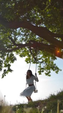 Sallanan genç bir kızın geniş görüşü. O kaygısız ve yeşil bir arazide uçmaktan mutlu. Hava açık ve bulutlu, mavi gökyüzü, gün batımı. Yeşil bir çayırın ortasında kocaman bir meşe ağacı. Dikey çekim