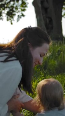 Beyaz rustik elbiseli genç ve güzel esmer anne kollarında küçük kızı alır ve alanın ortasında eski meşe ağacına doğru onunla yürür. Yavaş çekim. Orta görünüm