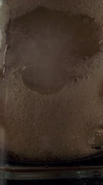Koyu renkli koladan oluşan yakın çekim akışı kafede buzla doldurulmuş cam bardak. Dikey çekim.