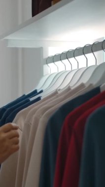 Elbise askılığında giysileri inceleyen genç bir bayanın yan görüntüsü, sonra da hafta sonu alışverişi sırasında kırmızı giysi seçmesi. Dikey çekim.