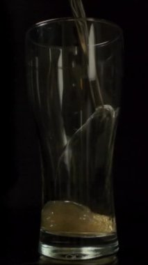 İnce bir damla taze bira bardağa dökülüyor ve bardağı karanlık odada yavaş çekimde taze soğuk birayla dolduruyor. Dikey çekim.