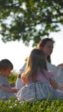 Genç bir anne ve iki küçük kızı yalnız bir meşe ağacının yakınındaki bir açıklıkta piknik yaptılar. Geniş açı. Kamera kızlara doğru hareket ediyor. Oyuncaklarını güvenli bir şekilde oynuyorlar. Ağır çekim. Dikey çekim