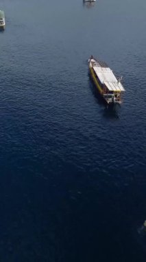 Tropik ada hava aracı. Lombok, gili. Okyanustaki tropikal adanın kıyı şeridi yakınlarındaki su üzerindeki teknelerin güzel manzarası. İHA hareketinde ön kule dikey çekim.