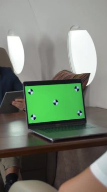 İş adamları uçağın içinde iş jetini tartışıyor. Yeşil ekran laptop monitörü için hazır. Lüks yaşam konsepti Kaypak bebek orta atışı. Dikey çekim.