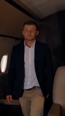 İş adamı güvenle ve destansı bir şekilde özel jetin içinde yürüyor. Lüks birinci sınıf uçak kabini pahalı koltuklar, ahşap masalar ve lombozlar. Dikey çekim.