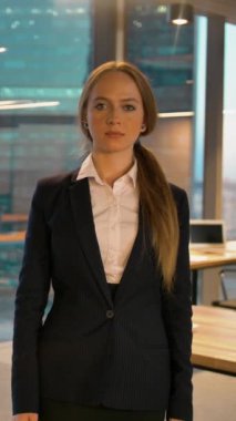 Resmi olarak kameraya poz veren iş kadını başparmağıyla işaret veriyor, modern iş alanı arka planı, büyük bina pencereleri. Yavaş çekim 4K çekimi. Dikey çekim.