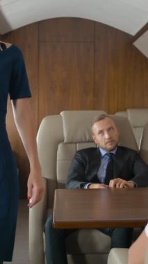 Özel jetin içindeki iş adamları uçuş sırasında dinleniyor ve hosteslerle konuşuyorlar. O, yolculara içecek ve yemeği sordu. Lüks hizmet. Dikey çekim.