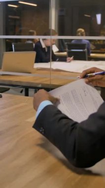 Toplantı odasında ciddi tartışmalar ve önemli belgelerin imzalanması. Afrikalı işadamı, toplantı sırasında ofisindeki müşteriye imza atması için belge veriyor. Dikey çekim.