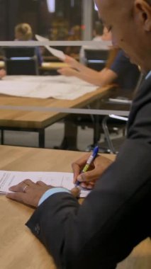 Afrikalı işadamı, toplantı sırasında ofisindeki müşteriye imza atması için belge veriyor. Toplantı odasında ciddi tartışmalar ve önemli belgelerin imzalanması var. 4k UHD Ağır çekim. Dikey çekim.