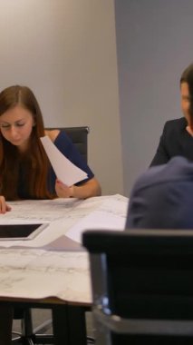 Mimarlar grubu planlı bir proje üzerinde çalışıyor. Masada büyük bir çizim var. Teknik sorunu çözmeye çalışan kendinden emin dört mühendis. 4k UHD. Dikey çekim.