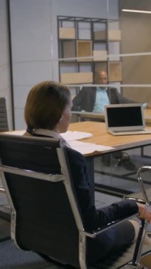 Genç ve çekici bir iş kadını koltuğunda kıvrılarak iş molasından zevk alıyor. Mutlu ve gülümsüyor. Yavaş çekim 4K UHD dikey çekim.