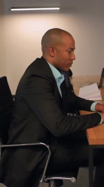 Ciddi Afrika kökenli Amerikalı genç adam internette çalışırken ve sörf yaparken dizüstü bilgisayar kullanıyor ve kameraya bakıyor. Yakın çekim teknoloji siyah iş çekici adam ağır çekimde dikey oturuyor