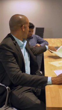 Afrikalı işadamı ve iş arkadaşı gece geç saatlere kadar ofislerinde dizüstü bilgisayarlarıyla çalışıyorlar. Koltukta oturuyor ve mobil bilgisayar defterine bazı arama etiketleri yazıyor. Dikey çekim.