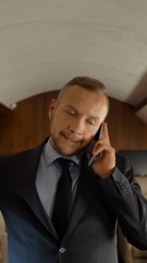 İş adamı iş görüşmesi için özel jetiyle seyahat ederken cep telefonuyla konuşuyor. Lüks seçkin birinci sınıf uçak kabini iç mimarisi. Dikey çekim.