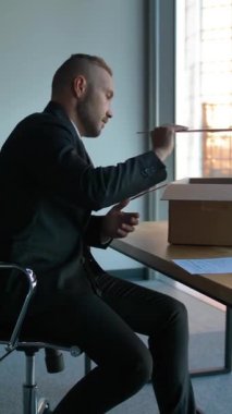 Ofisinde taşınma kutusu olan, bavullarını boşaltan, büyük cam pencereli modern ofis girişimcisi. 4k UltraHD yavaş çekim. Dikey çekim.