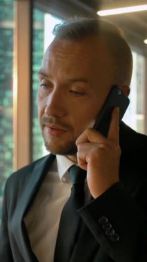 İş yerindeki çekici işadamının portresi anlaşma ortağını çağırıyor. Önemli bir cep telefonu görüşmesi, ciddi bir iş konsepti. Dikey çekim.