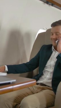 Zengin girişimci, cep telefonu ortağı Connect uçak seyahati ile konuşuyor. Cep telefonu ve dizüstü bilgisayarla mutluluk ve iyi ruh haliyle olumlu bir konuşma yaptı. 4K UHD dikey çekim.