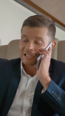 Zengin, mutlu, olgun iş adamının yakın çekimi ve cep telefonuyla konuşma ve iş jetinde seyahat ederken defter üzerinde çalışma. Dikey çekim.