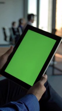 Latin iş adamı, çağrı merkezindeki modern çalışma ofisinde elinde yeşil ekranlı siyah tablet bir bilgisayar tutuyor. Krom anahtar. İzleme görüntülerine hazırız. Dolly kamera hareketi 4k ağır çekim. Dikey