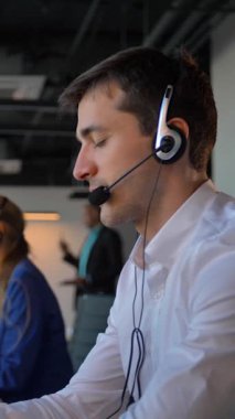 Kulaklık takmış çekici bir iş adamı iş merkezindeki şapşalları arıyor. Bayan meslektaşları da müşterileriyle telefonla iletişim kuruyor. 4k ağır çekim, dikey çekim.