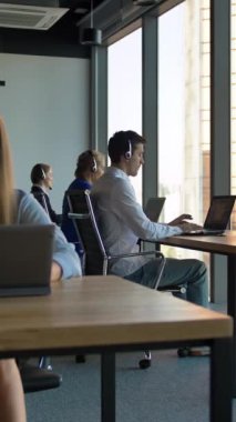 Genç çekici iş kadını portresi çağrı merkezini kontrol ediyor. Kameraya bakarken gülümsüyor. Modern binanın içinde, iş alanı penceresi manzaralı. Kaydırma hareketi. Dikey çekim.