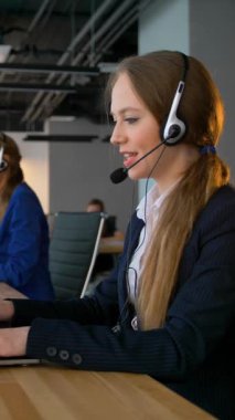 Çağrı merkezi iş kadını müşterilerle sohbet ediyor. Dizüstü bilgisayara bakıyor ve sonra da gülümseyerek kameraya bakıyor. Modern ofis iş merkezi. Orta çekim. 4k yavaş çekim dikey çekim.
