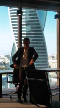 Modern iş ofisinde cam duvarlı ve kapılı dans eden erkek işadamı silueti. Keyfi yerindeyken mutlu bir şekilde dans ediyor çünkü hafta sonu geliyor. 4k yavaş çekim dikey çekim.