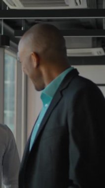 Patron ve çalışanlar yeni ofiste kutularla çalışmaya başlıyorlar. Siyah tenli Afro-Amerikan patronu modern ofislerdeki meslektaşlarını cam pencereli cesaretlendiriyor. Ağır çekim. Dikey çekim.