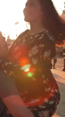 Günbatımı caddesinde dans eden genç çift. Lenslerden çıkan turuncu ışıklar. Gülümseme, gülme, mutluluk, açıklık yoldan geçenlerin önünde utanma. Ortadaki 4 km yavaş çekim. Dikey çekim.