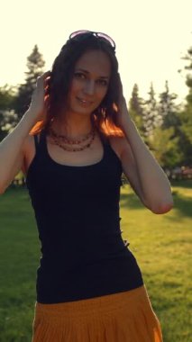 Gün batımında ya da gün doğumunda parkta gülümseyen bir kadın portresi. Kızıl saçlı kızıl. 4k Ağır çekim. Dikey çekim.