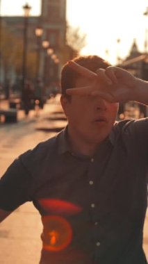 Şehir caddesinde dans eden mutlu, gülümseyen erkek portresi. Genç ve çekici bir adam şehirde eğlenmek için kulübe gidiyor. Gün doğumu. Dikey çekim.