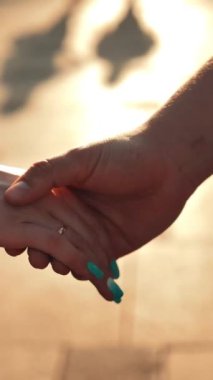 Gün batımında birbirine sarılan iki el. Erkek ve kadın aşıklar kollarına dokunuyor. Dikey çekim.