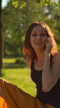 Happy, şehir parkında yeşil çimlerde oturan ve dijital akıllı telefon cihazıyla arkadaşça sohbetin keyfini çıkaran bir kadın buldu..