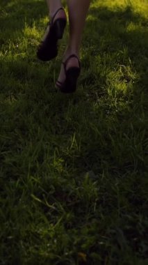 Parkta çimlerin üzerinde koşan kadın ayakları. Yüzü yok. Gün batımı ya da yüzey. Süper yavaş çekim. Orta etek, ince bacaklar. Dikey çekim.