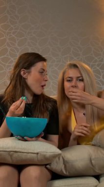 Akşam elbiseleri içinde üç güzel genç ve gülümseyen kız evdeki kanepede televizyon ya da film izleyip patlamış mısır yiyorlar..