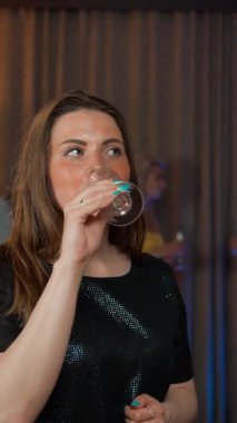 İki seksi ve çekici genç bayan, kadeh tokuşturulmuş şarapla dedikodu yapıyorlar. Partide konuşmaktan memnunlar. 4k UHD. Dikey çekim.