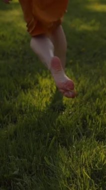 Parkta çimlerin üzerinde koşan bayanlar. Yüzü yok. Gün batımı ya da yüzey. Gerçek zamanlı ve yavaş çekim karışık görüntüler. Orta etek, ince bacaklar, yalın ayak. Dikey çekim.