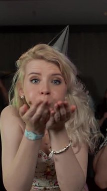 Genç ve güzel bir çift yeni yıl partisinde eğleniyor, parti şapkaları takıyor, dans ediyor ve parti düdüğü çalıyor. Stüdyo ışıkları. Tatilde tebrik ederim. Süper yavaş çekim dikey çekim.