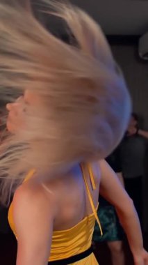 Sarışın güzel bir kadın sarı elbiseyle dans ediyor. Seksi parti dansı süper yavaş çekim. Gülümseme ve mutluluk alkollü ev partisi. Dikey çekim.