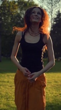 Uzun kırmızı etekli genç bir kadın parkta zıplıyor ve dışarıda dans ediyor. O, zaman geçirmekten mutlu. Gün doğumu ya da batımı güzel bir ışık. Dikey çekim.