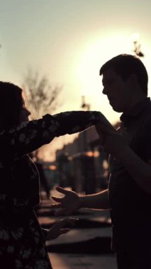 Şehirdeki büyük yolda dans eden genç çift siluetleri ve arka planda günbatımı güneşi. Karanlık gölgeler, aşıkların tanınabilir yüzleri yok. Ağır çekim. Dikey çekim.